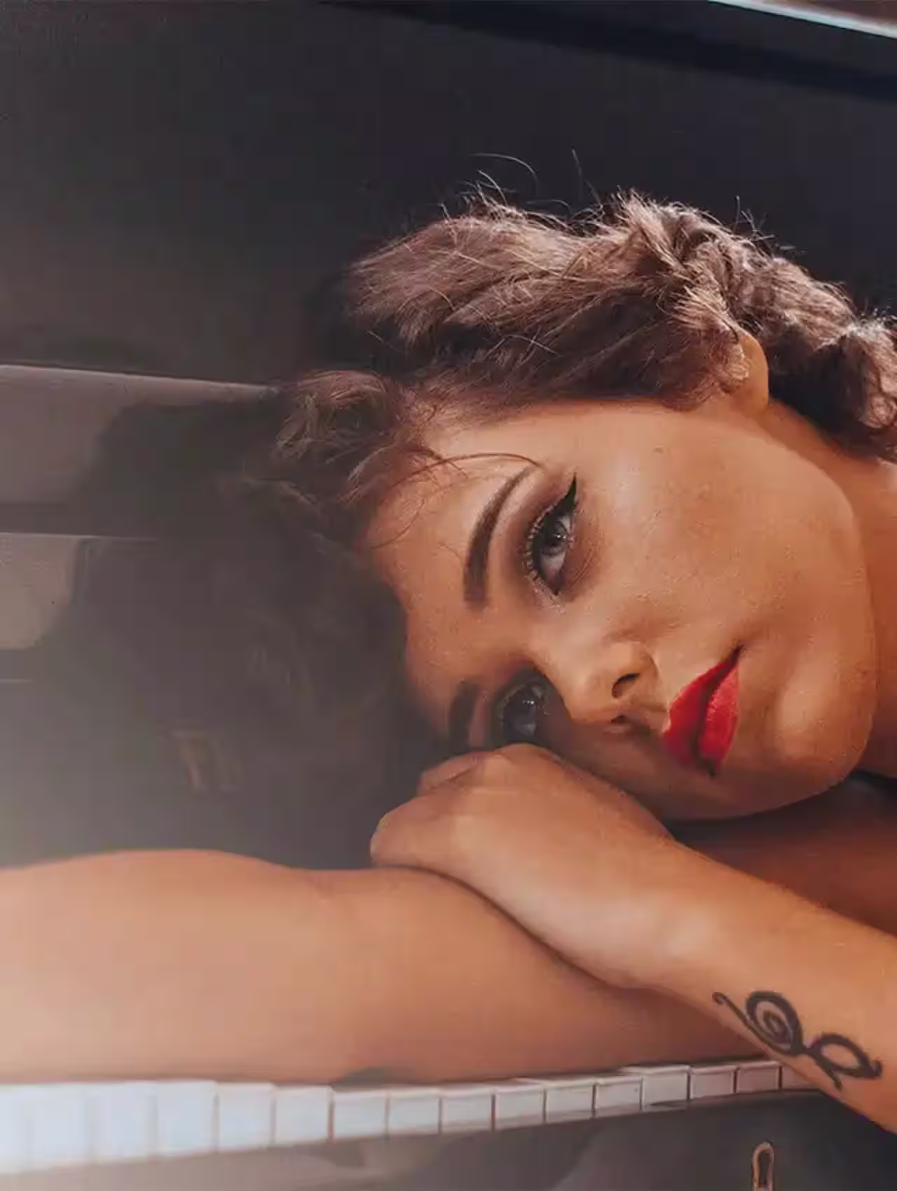 Mujer con mirada melancólica apoyada sobre un piano, representando un corazón roto y el inicio de la sanación.
