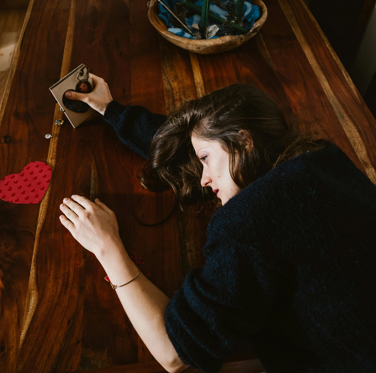 Mujer acostada en una mesa abrazando una foto, reflejando tristeza y corazón roto tras una ruptura amorosa.