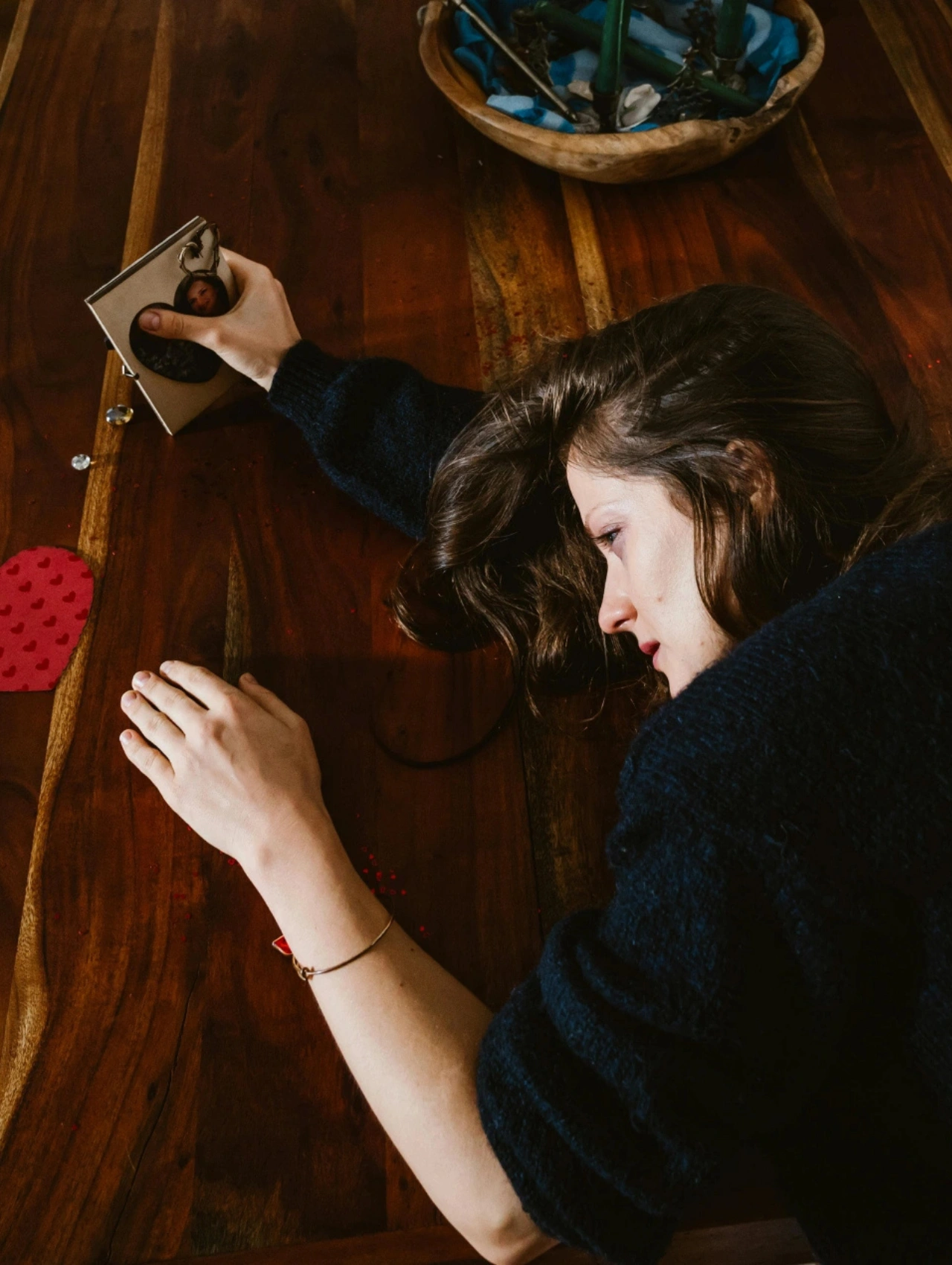 Mujer recostada sobre una mesa sosteniendo una foto, reflejando tristeza y duelo por un corazón roto.