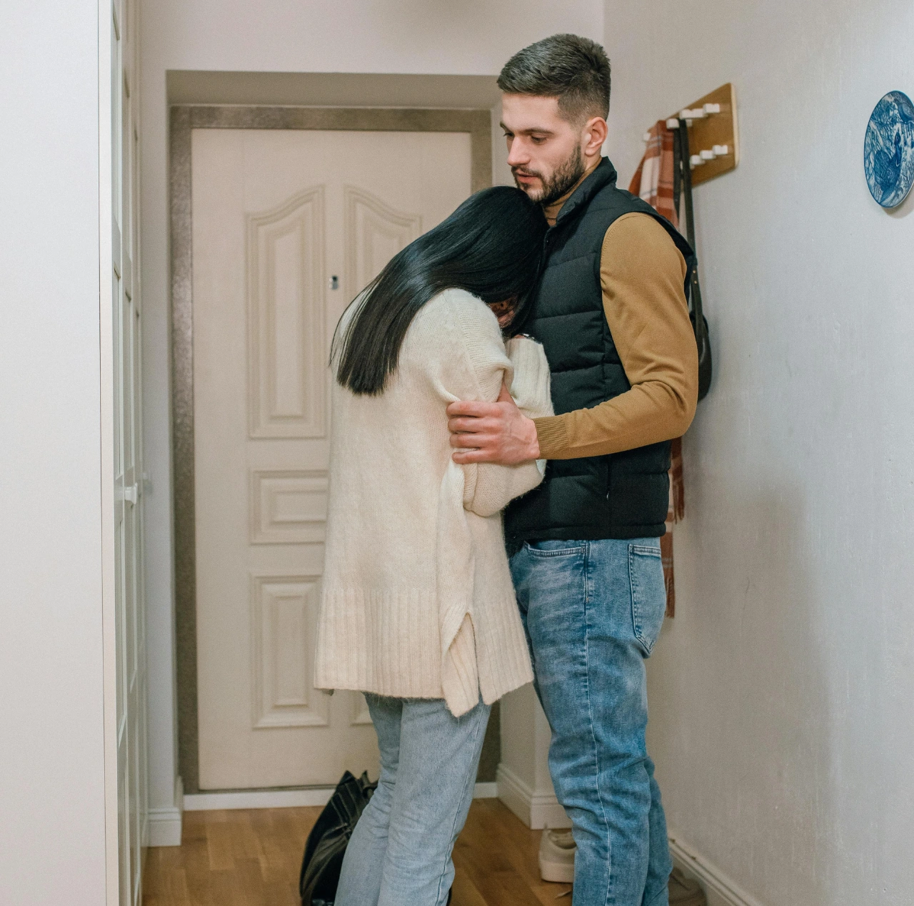 Una pareja abrazándose en la puerta durante una despedida emocional, representando un momento de corazón roto.