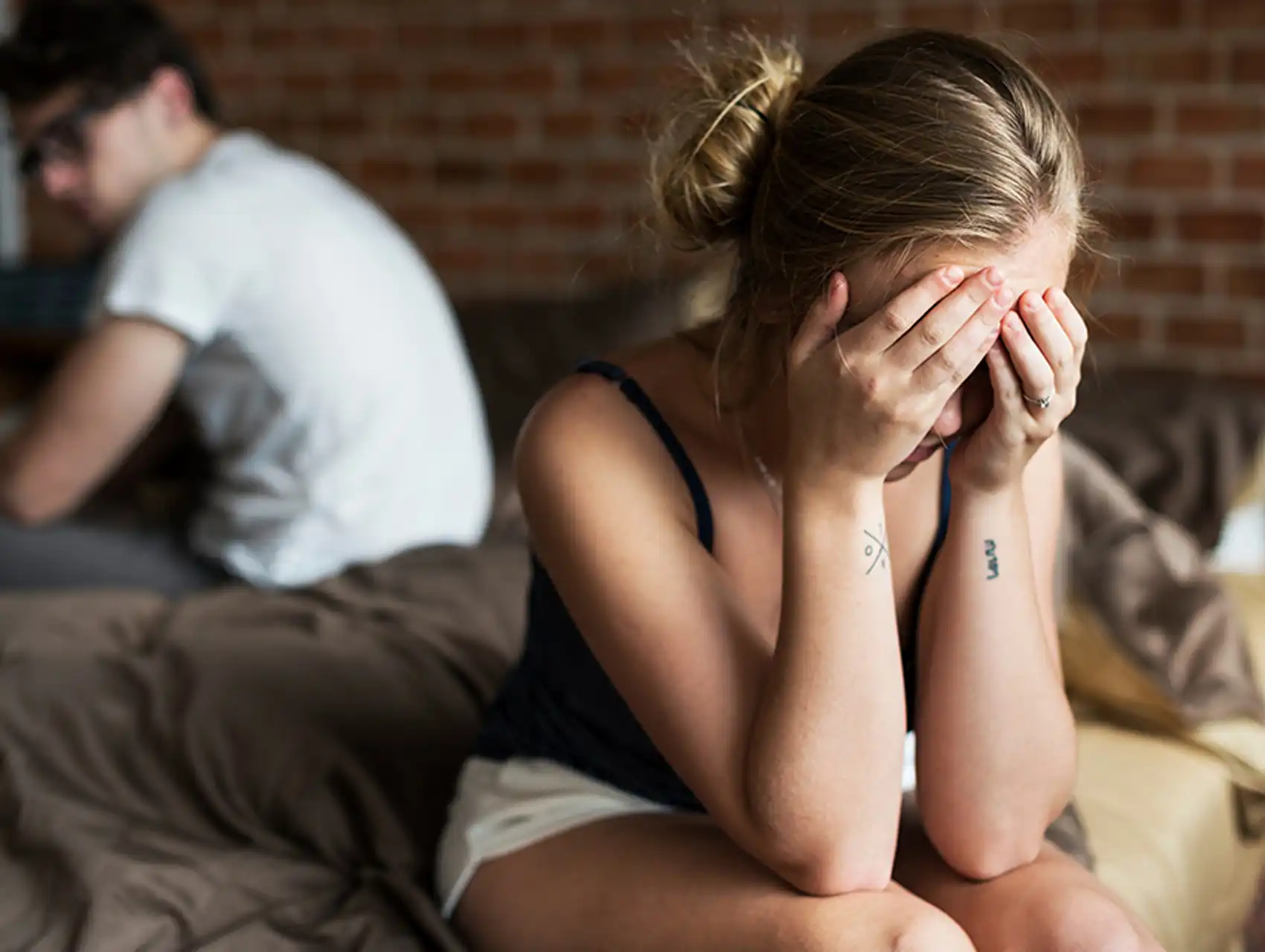 Mujer angustiada con las manos en la cara tras discusión con su pareja en la cama, problemas de pareja