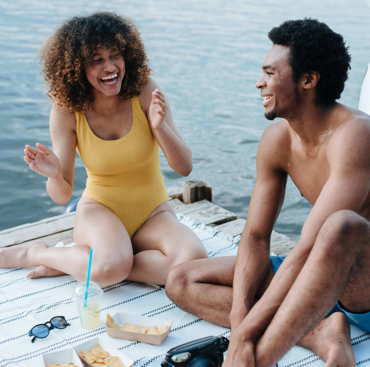 Pareja conversando y riendo en un muelle junto a un lago, ilustrando comunicación efectiva y asertiva.