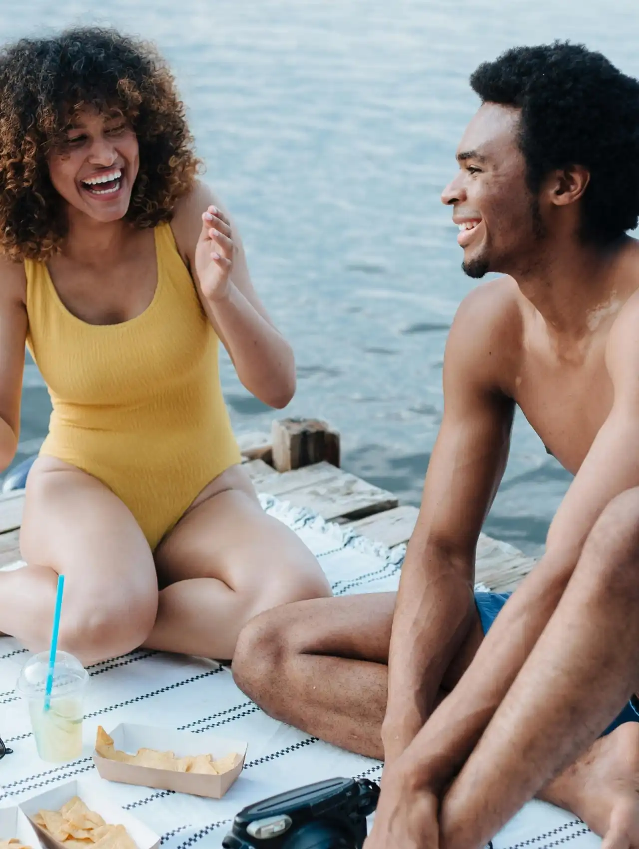Pareja joven disfrutando al aire libre con comunicación efectiva y asertiva, compartiendo risas en un muelle.