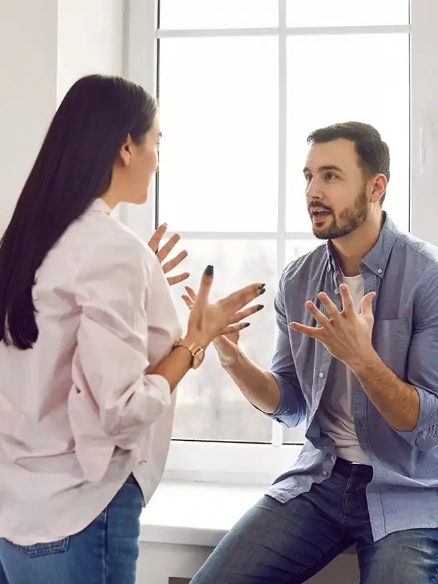 Pareja discutiendo intensamente frente a una ventana, mostrando red flags en una relación