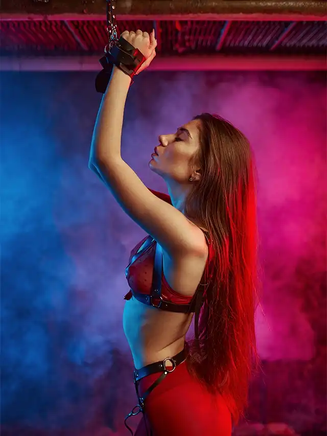 Mujer con arnés de cuero rojo colgada de cadenas, representando juegos de dominación y fetiches sexuales más comunes.