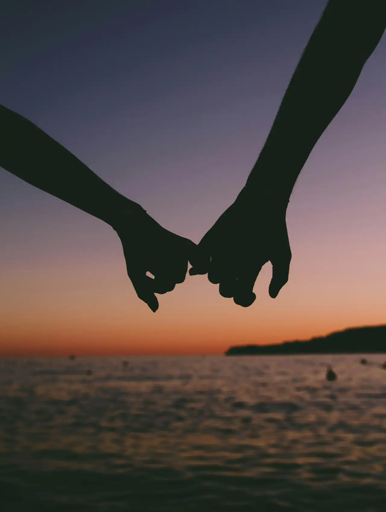 Pareja entrelazando los dedos al atardecer junto al mar, representando el apego en las relaciones de pareja.