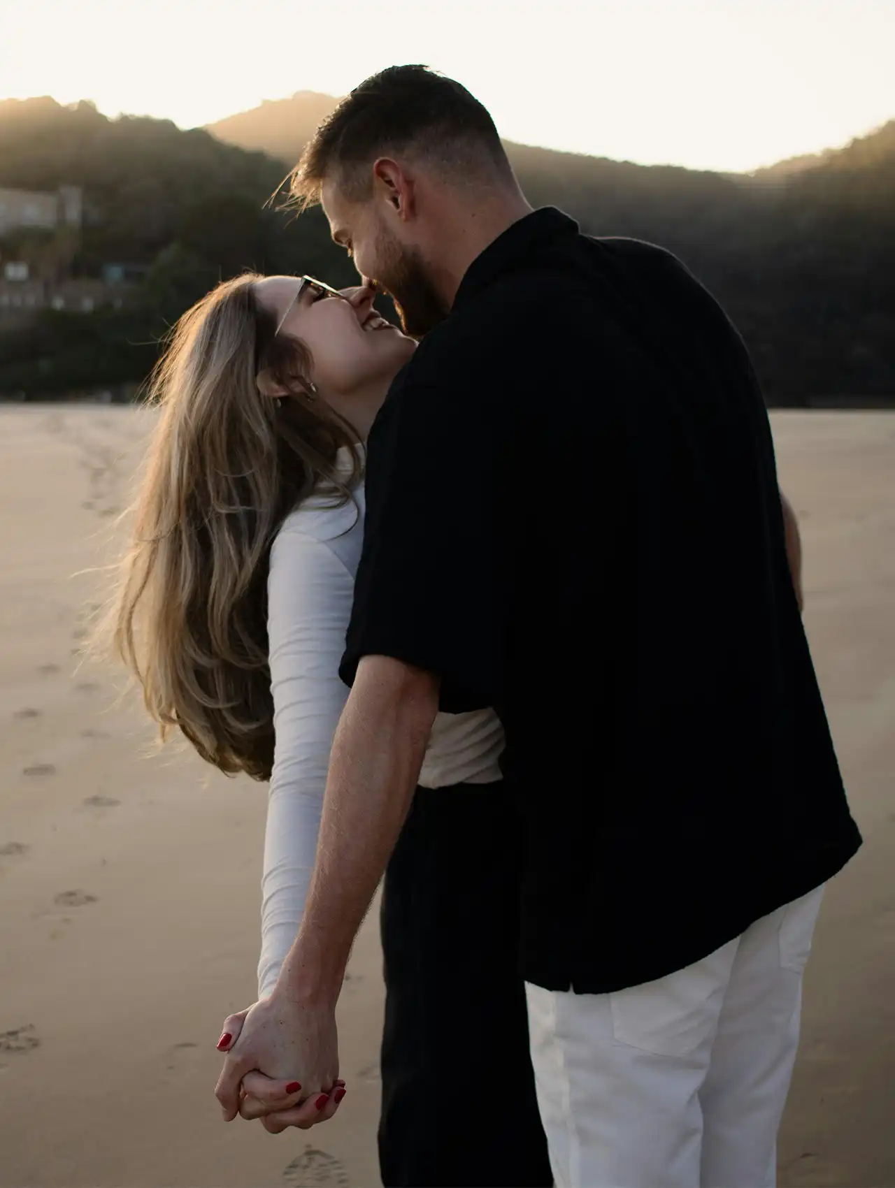 Pareja abrazándose y sonriendo en la playa al atardecer, simbolizando metas de pareja.