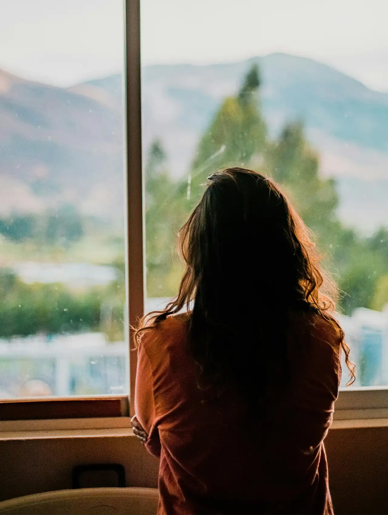Mujer mirando por la ventana con vista a la montaña — consecuencias de tomar anticonceptivos por muchos años