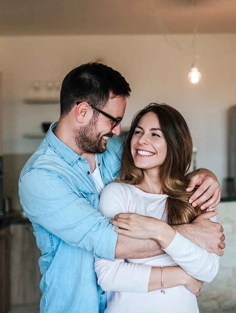 Pareja sonriente abrazándose en la cocina tras resolver una discusión – como resolver una pelea de pareja