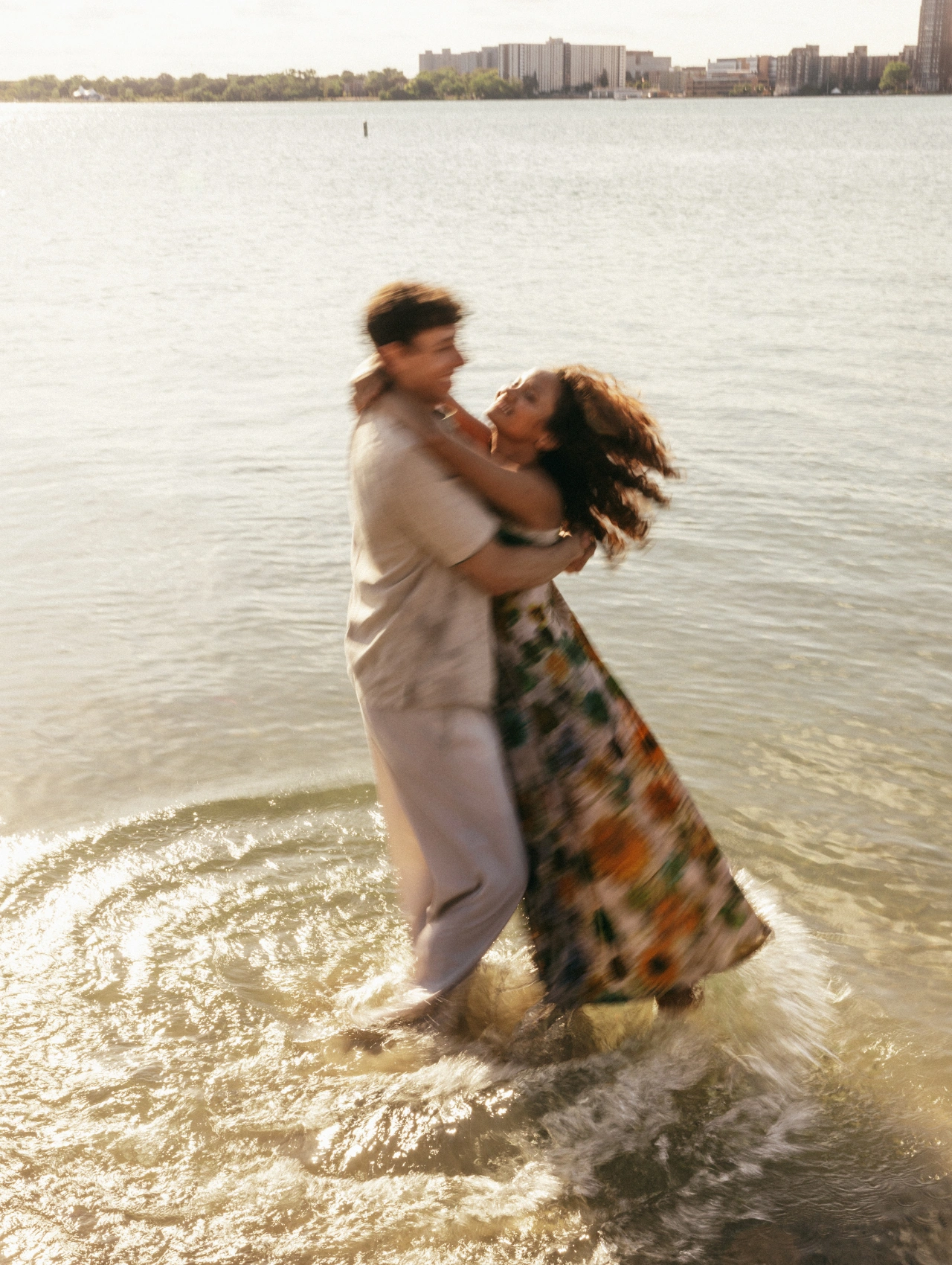 Pareja girando con alegría en el agua durante un momento íntimo al aire libre, reflejando la espontaneidad del amor romántico.