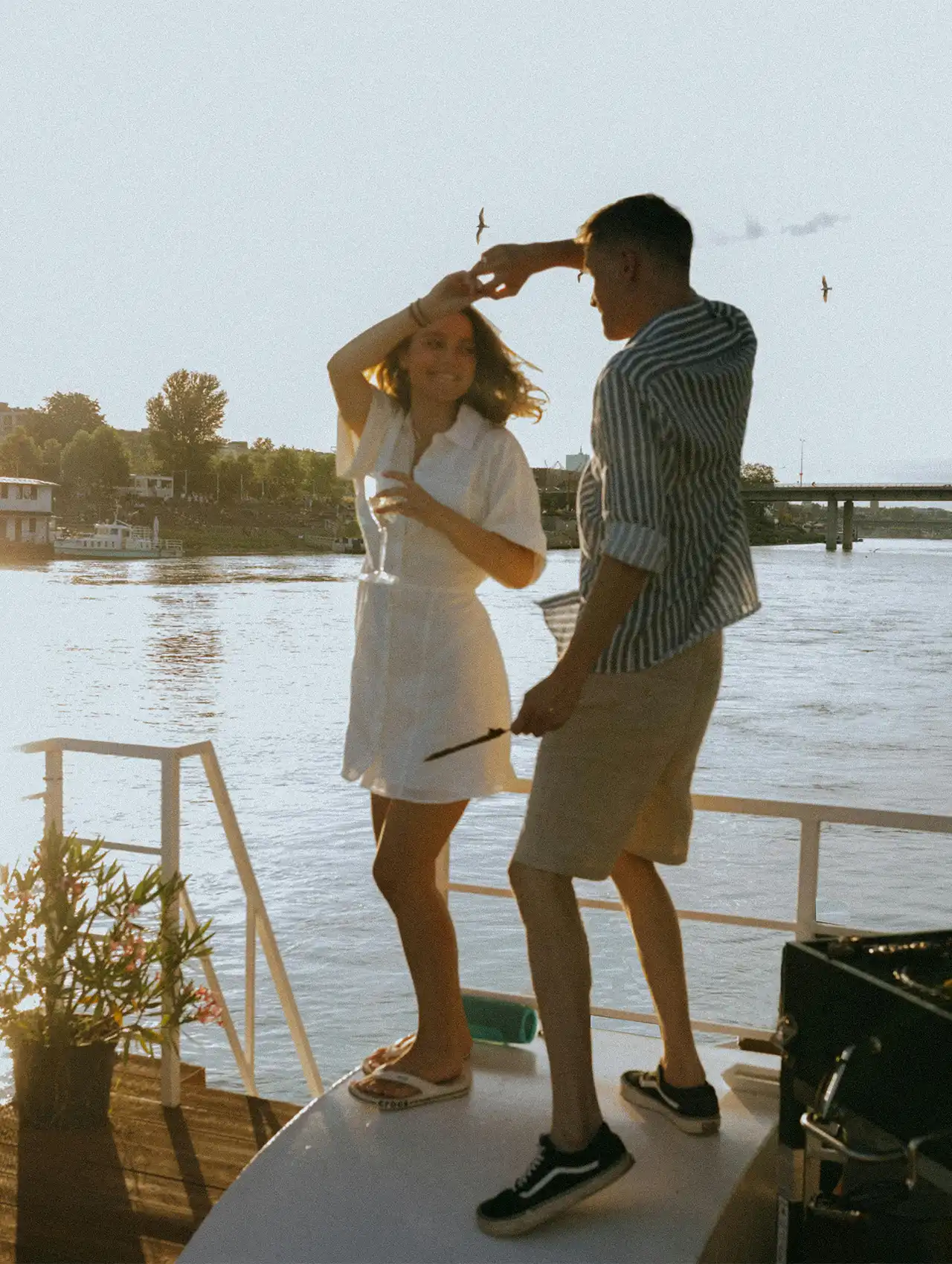 Pareja bailando sobre un barco al atardecer, con copa en mano, citas románticas