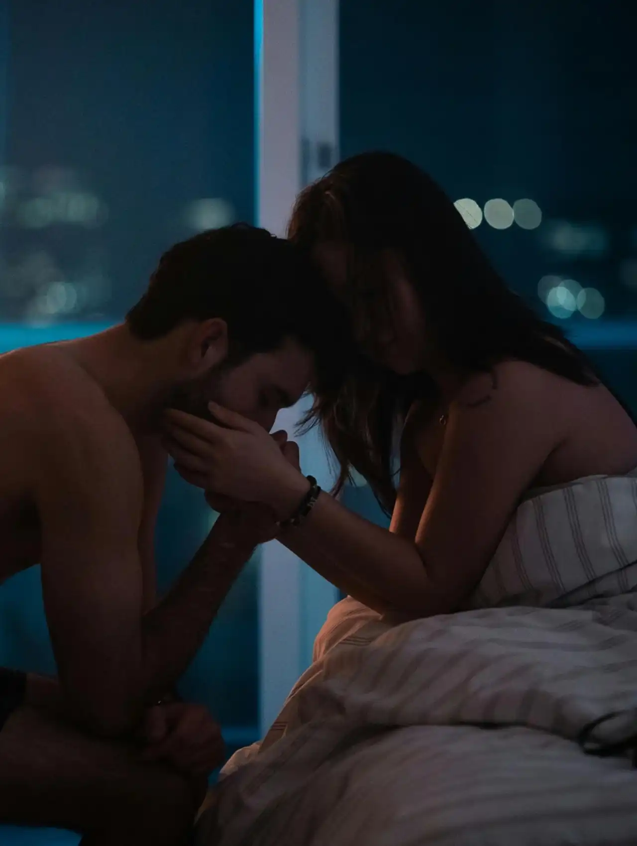 Hombre besando la mano de su pareja en una habitación de noche, simbolizando como recuperar la confianza en tu pareja con gestos de respeto.