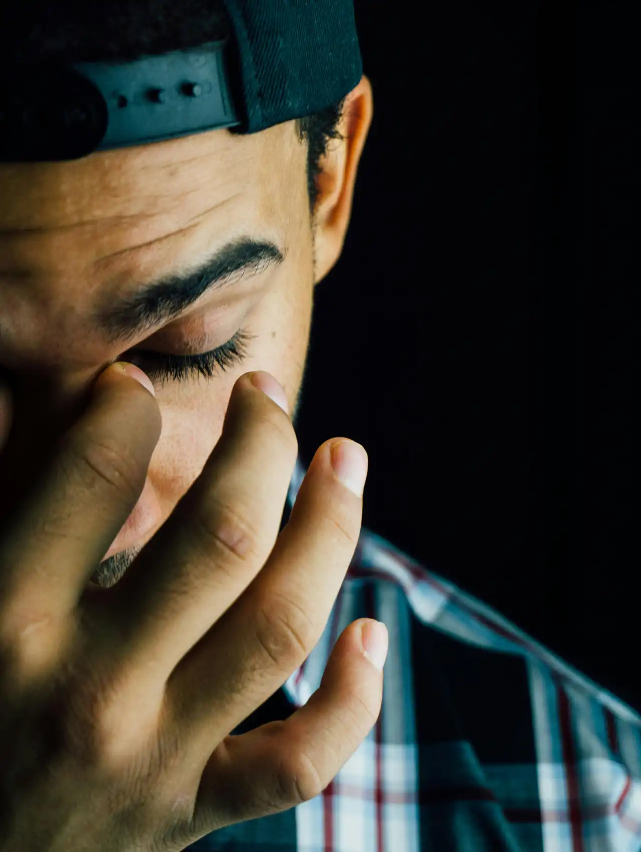 Hombre con gorra y camisa a cuadros cubriéndose el rostro, simbolizando tristeza y el reto de cómo recuperarse de una infidelidad de mi esposa.