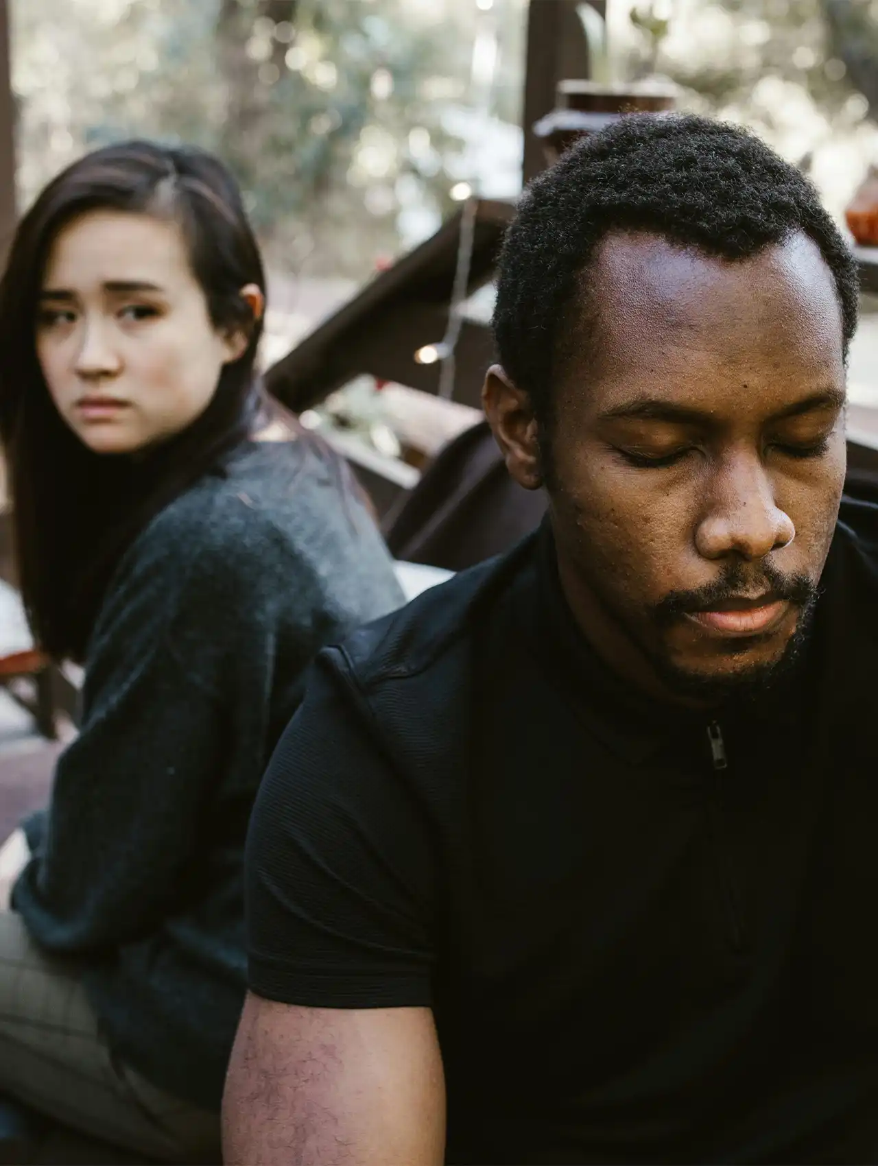 Pareja sentada al aire libre, ambos con gestos serios y distantes, reflejando la dificultad de cómo recuperarse de una infidelidad de mi esposa.