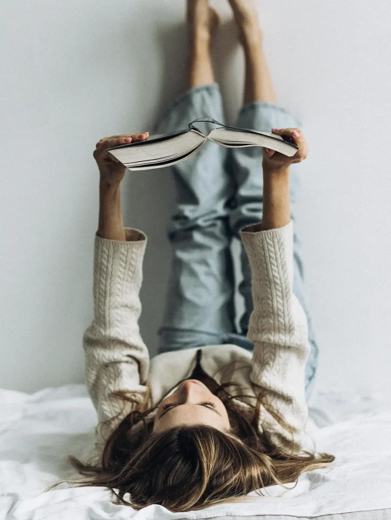 Joven acostada leyendo un libro, ideal para ilustrar momentos de lectura de libros de romance juvenil.