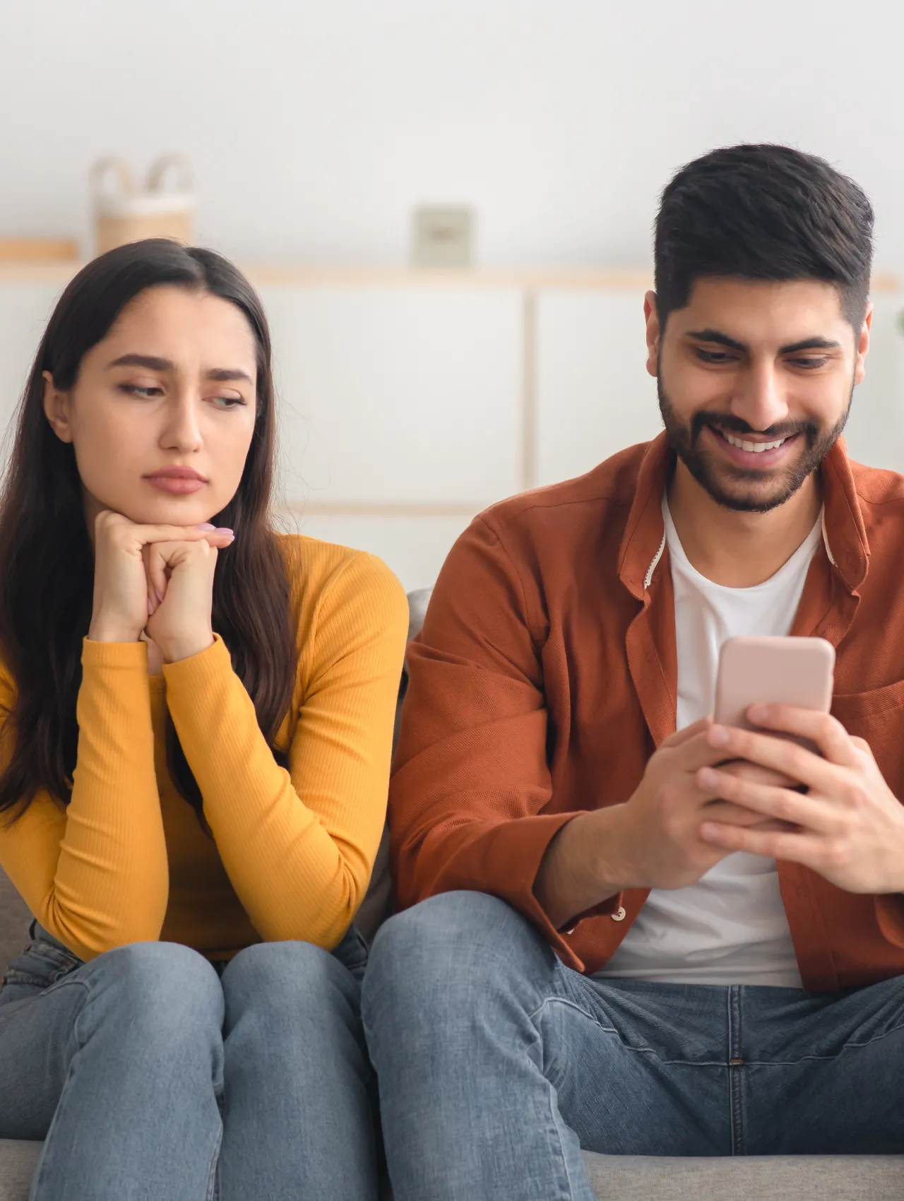 Mujer observando con desconfianza a su pareja mientras él sonríe con el teléfono, reflejo de red flags en una relación.