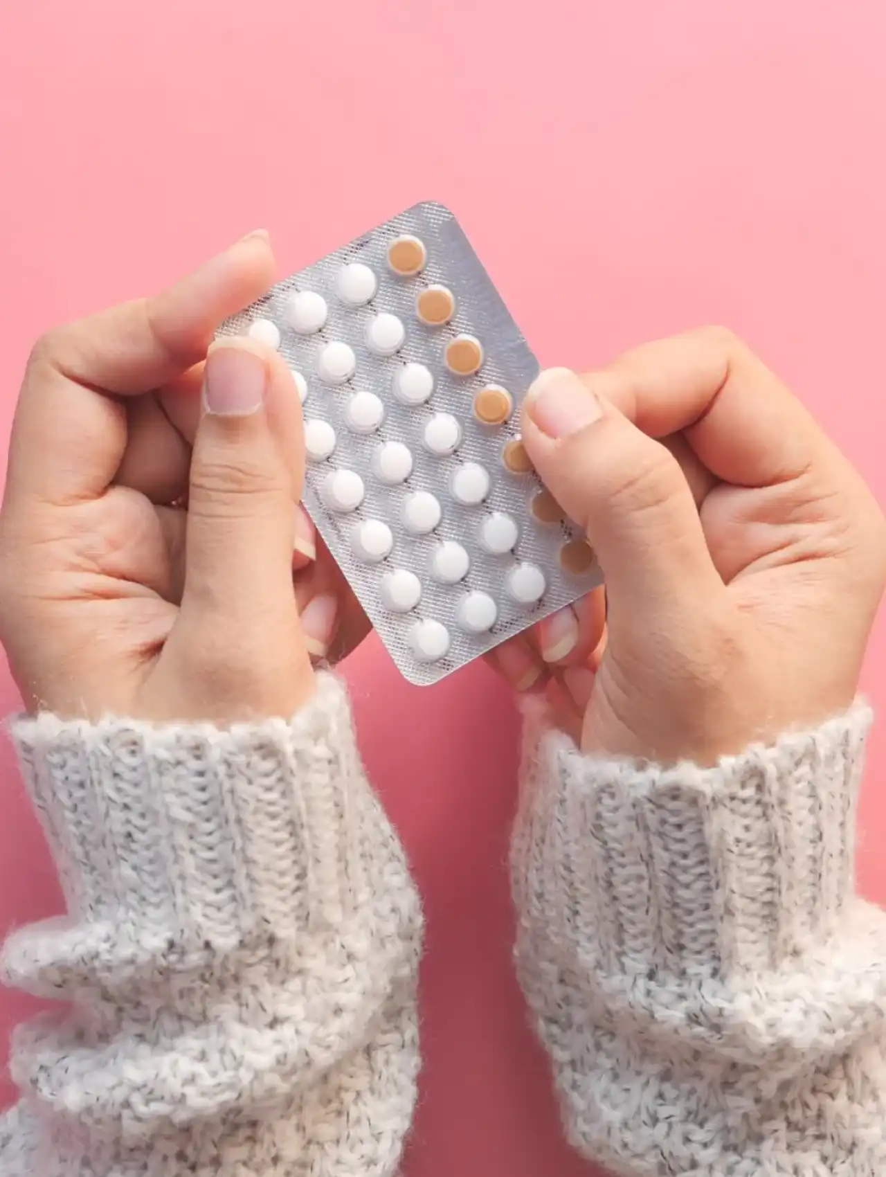 Manos sosteniendo blíster de píldoras anticonceptivas sobre fondo rosa — cuales son las mejores pastillas anticonceptivas