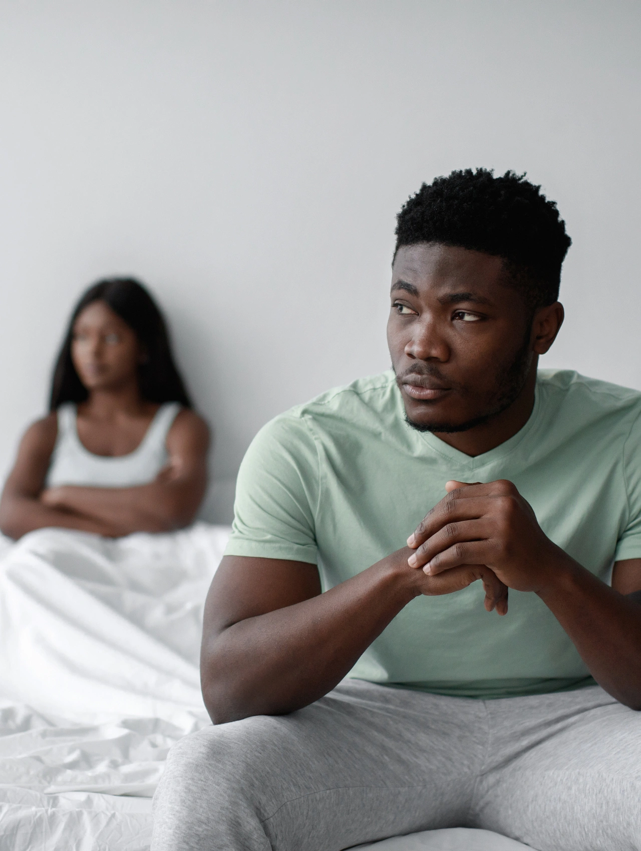 Hombre sentado con expresión serena mientras su pareja aparece al fondo, transmitiendo calma y seguridad en la relación, relacionado con cómo saber si un hombre te es fiel, mostrando que te da tranquilidad, no ansiedad.