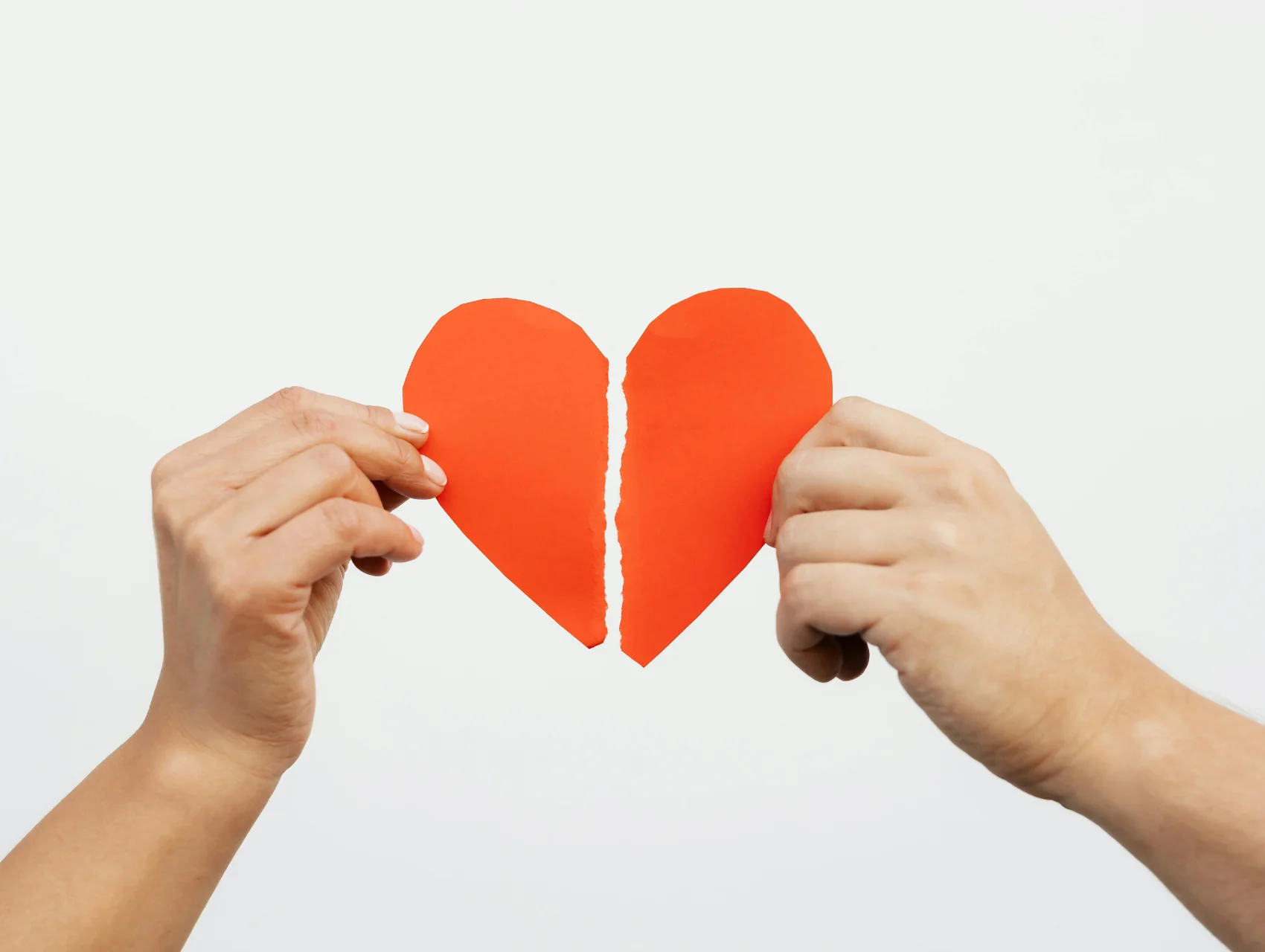 Dos manos separando un corazón de papel naranja sobre fondo blanco, el desgaste emocional cuando un hombre pierde el interés en una mujer