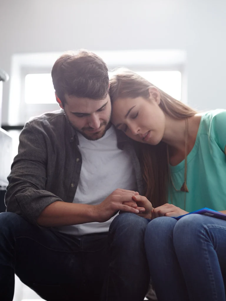 Mujer apoyando su cabeza en el hombro de su pareja mientras sostienen las manos, escena que representa la dependencia emocional frente al amor sano en una relación de pareja.