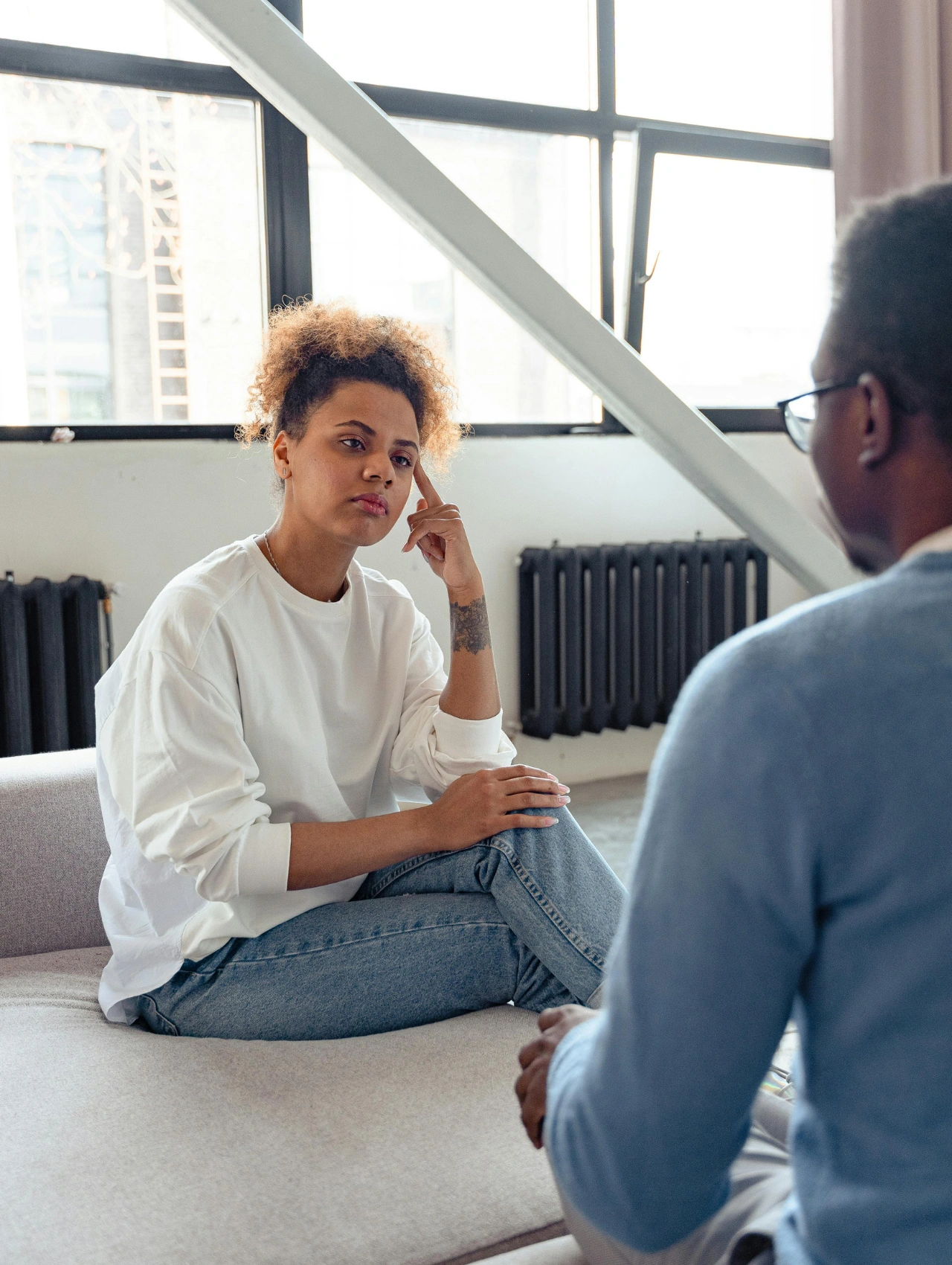 Mujer sentada frente a su pareja con gesto serio y distante durante una conversación difícil, ejemplo de red flags en mujeres cuando los celos no se dicen pero se interpretan en el lenguaje corporal
