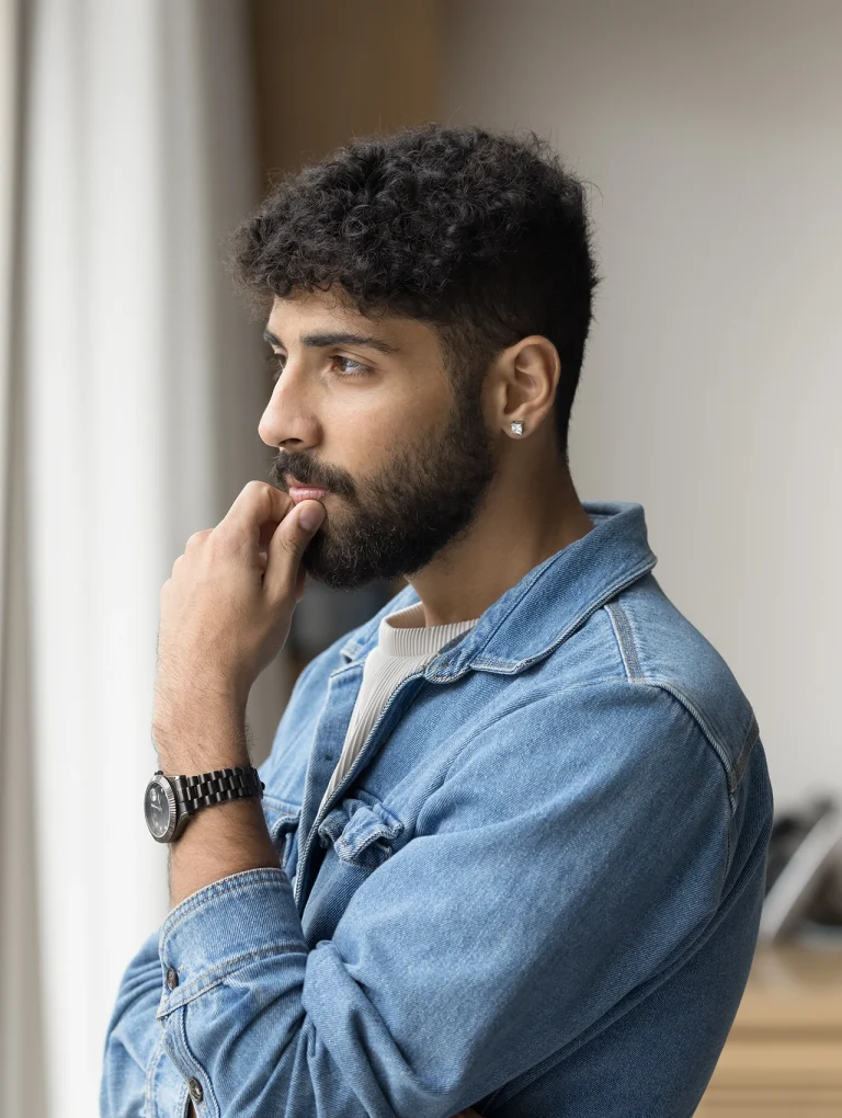 Hombre joven con expresión pensativa apoyando la mano en el rostro, representando el bloqueo emocional en hombres cuando no saben qué sienten, pero perciben que algo no está bien a nivel emocional.