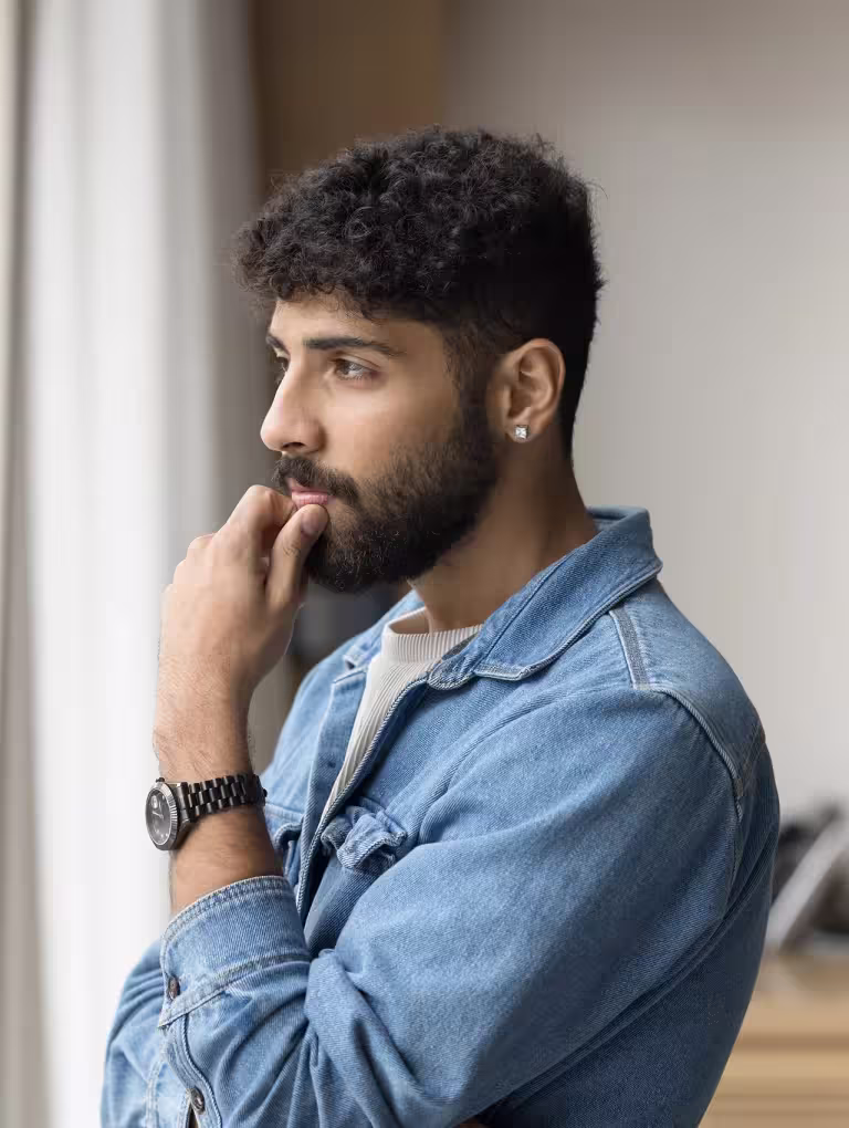 Hombre joven con expresión pensativa apoyando la mano en el rostro, representando el bloqueo emocional en hombres cuando no saben qué sienten, pero perciben que algo no está bien a nivel emocional.