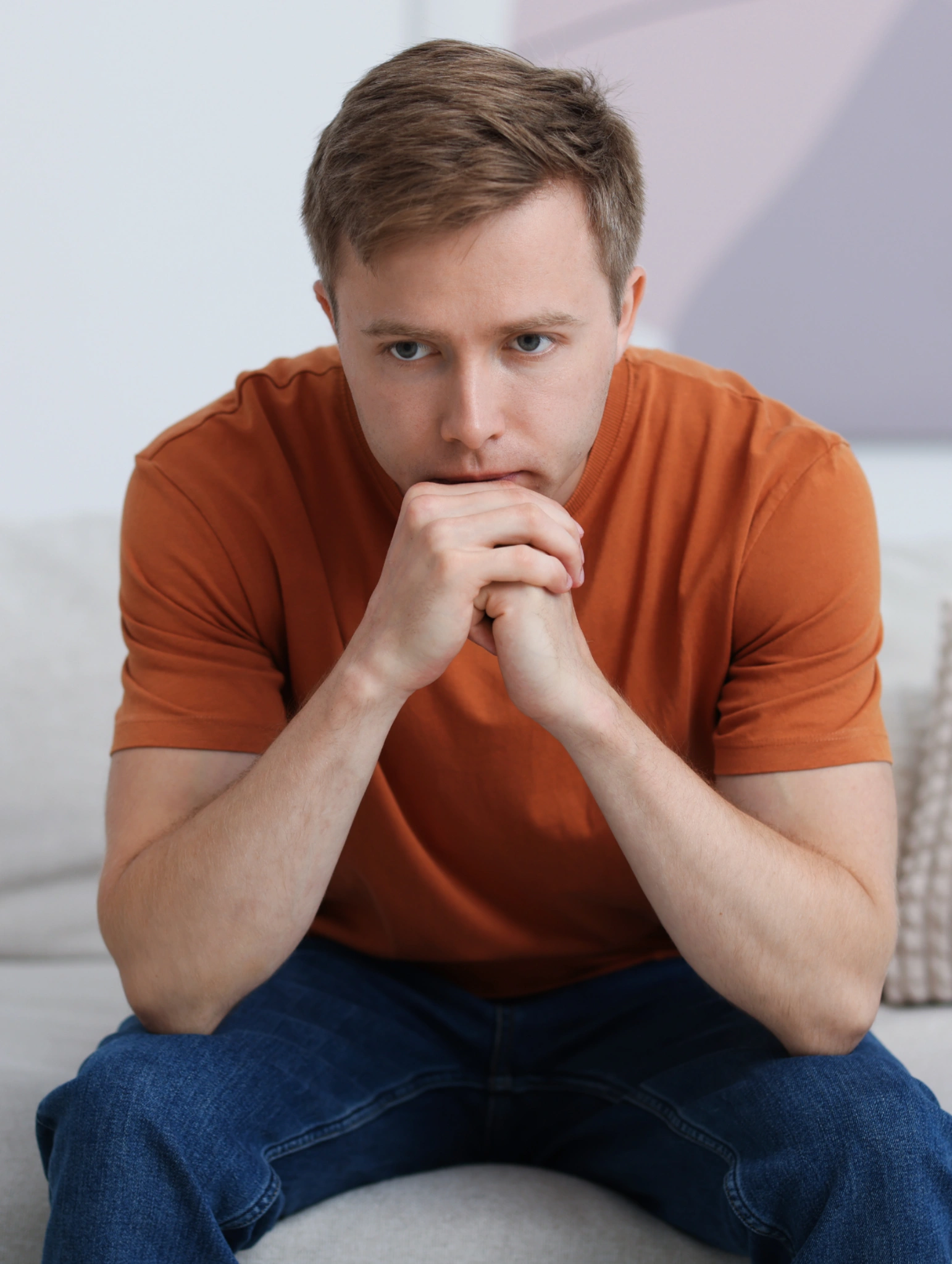 Hombre joven sentado con expresión reflexiva y gesto serio, representando los mitos y dudas al pensar cuáles son los condones más seguros y si afectan el placer durante las relaciones.