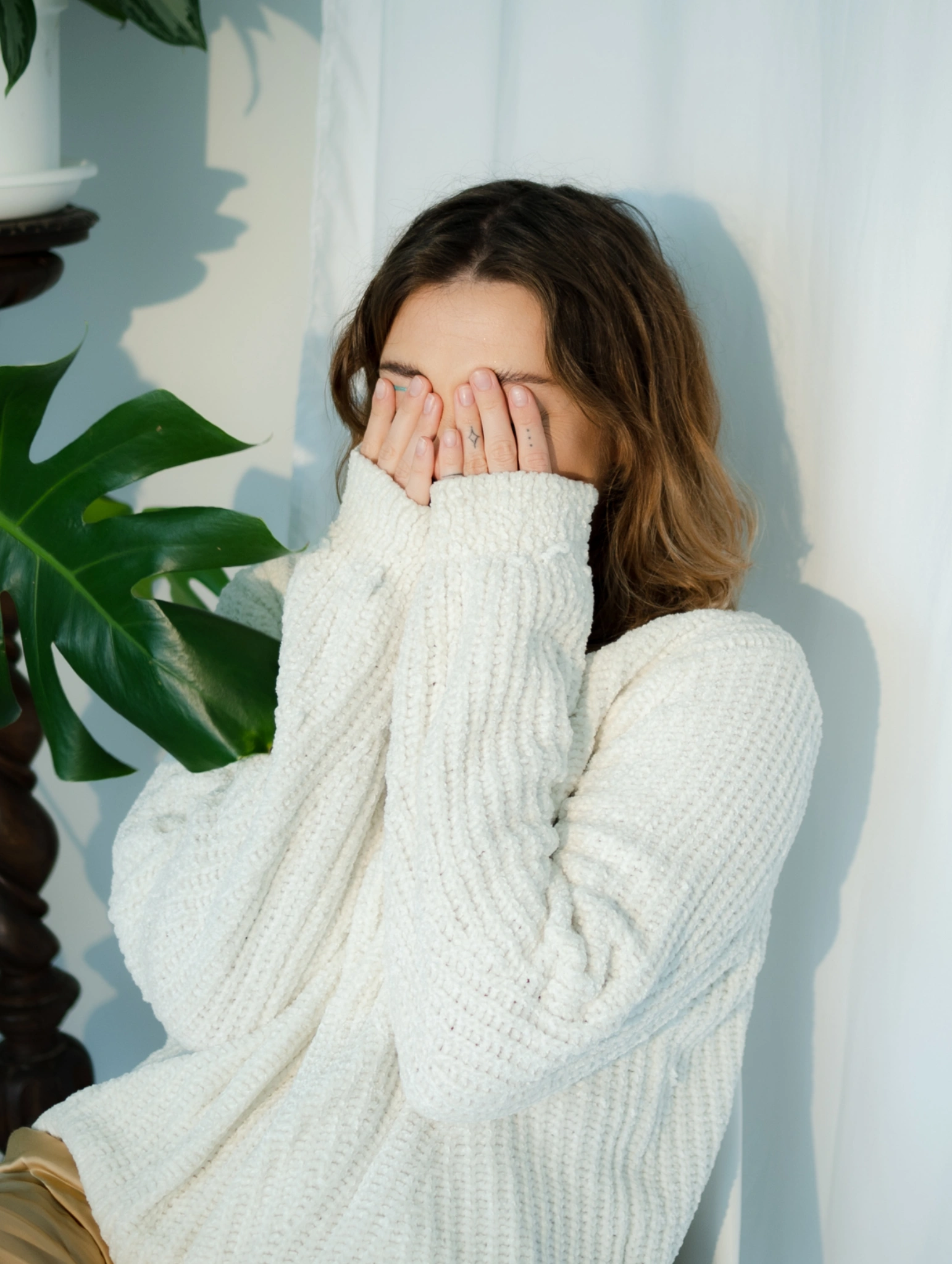 Mujer con suéter blanco cubriéndose parte del rostro con las manos, expresión tímida y nerviosa, imagen que representa cómo coquetear con un chico cuando se siente intenso o abrumador.