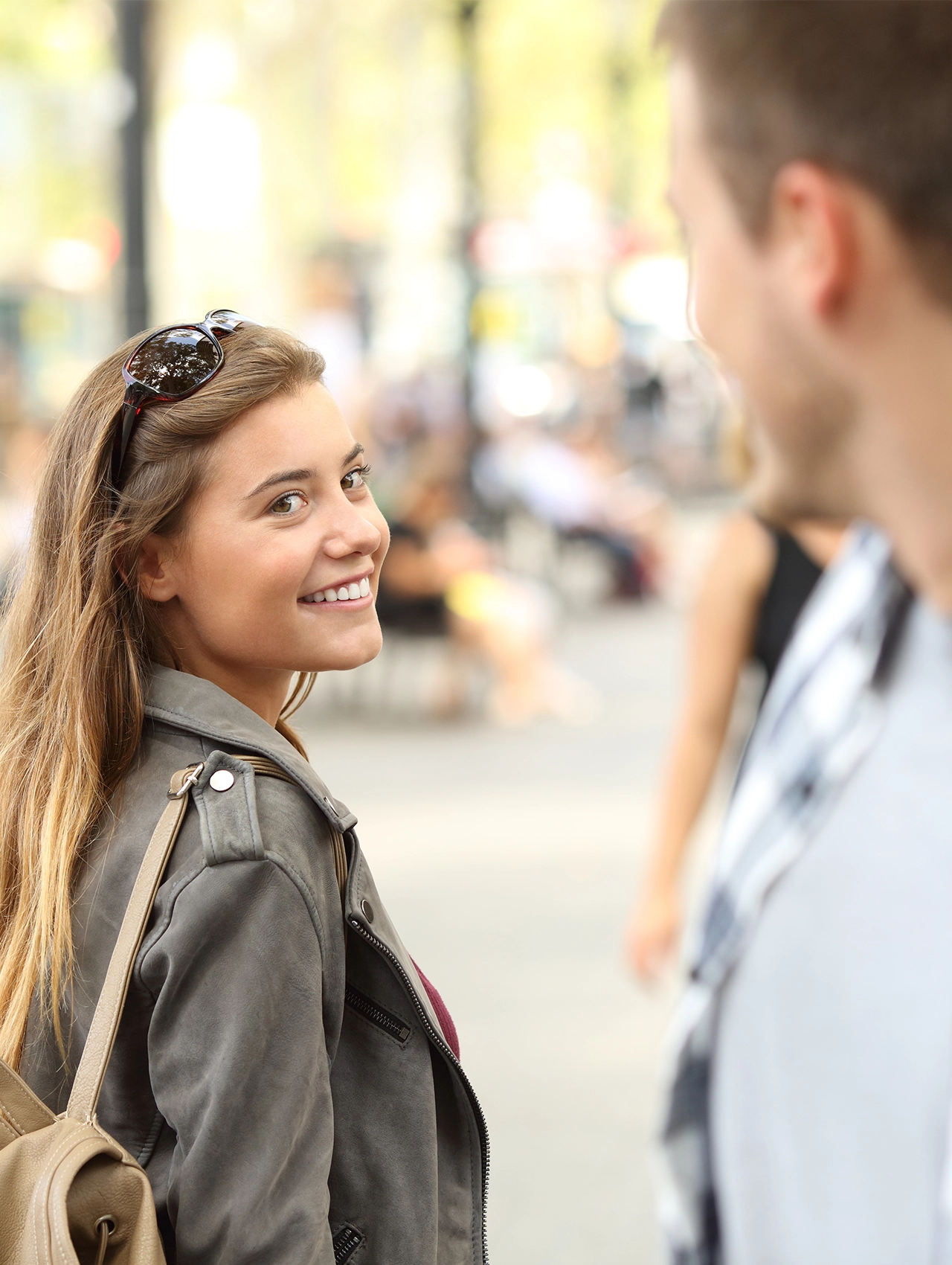 Mujer sonriendo y mirando hacia atrás en una calle mientras conversa con un hombre, escena ideal para ilustrar cómo coquetear con un chico de forma natural y segura.