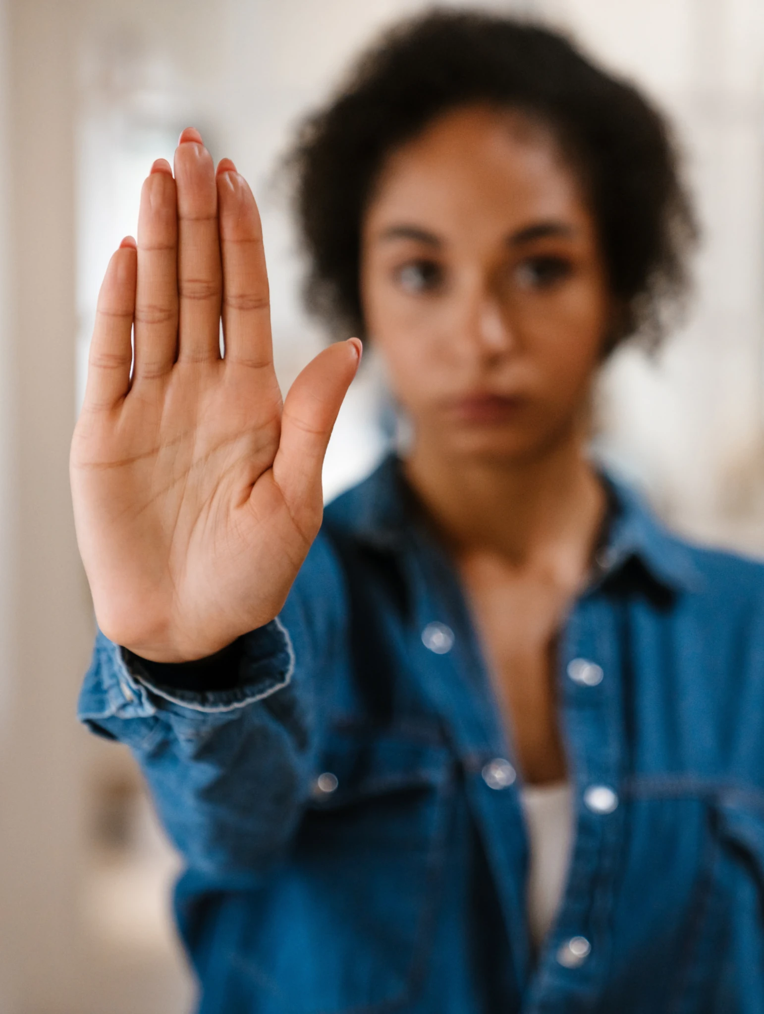 Mujer con camisa de mezclilla levanta la mano en señal de “alto”, gesto de límites ante el gaslighting y la manipulación emocional en una relación.