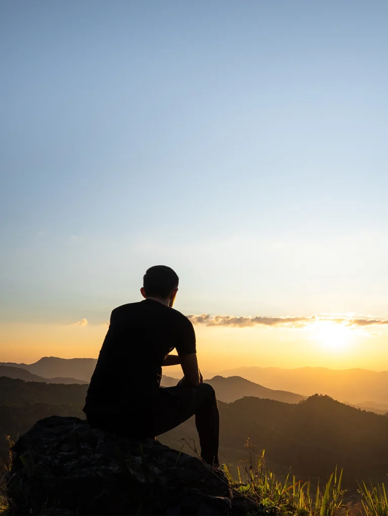 Apego evitativo en un hombre sentado solo frente a las montañas al atardecer, reflejando distancia emocional y aislamiento.