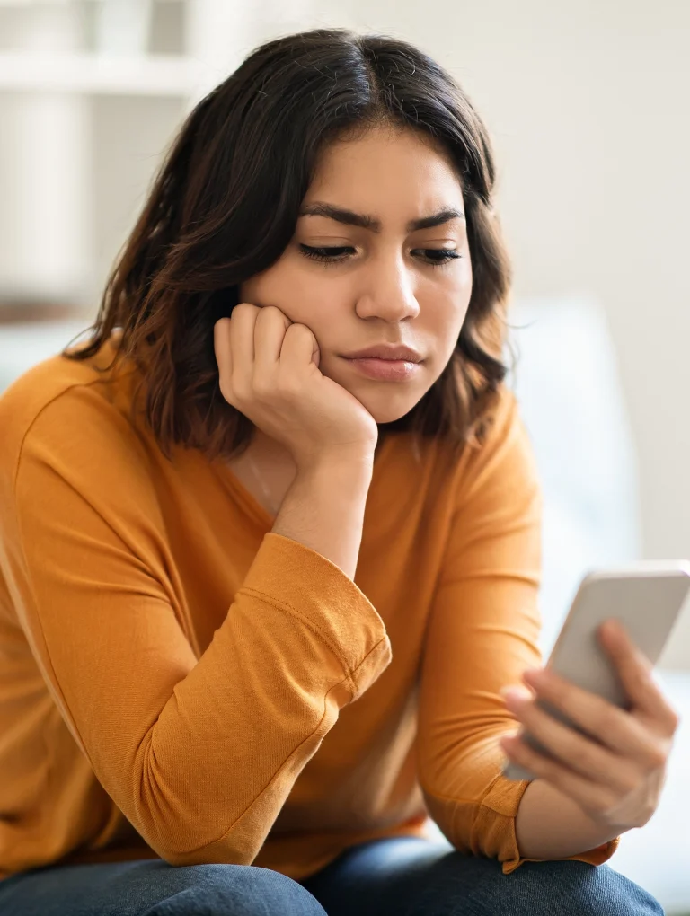 Mujer mirando su celular con expresión triste y pensativa, representando cómo terminar una relación a distancia cuando la conexión emocional comienza a romperse.