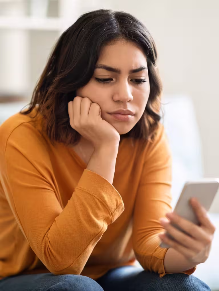 Mujer mirando su celular con expresión triste y pensativa, representando cómo terminar una relación a distancia cuando la conexión emocional comienza a romperse.