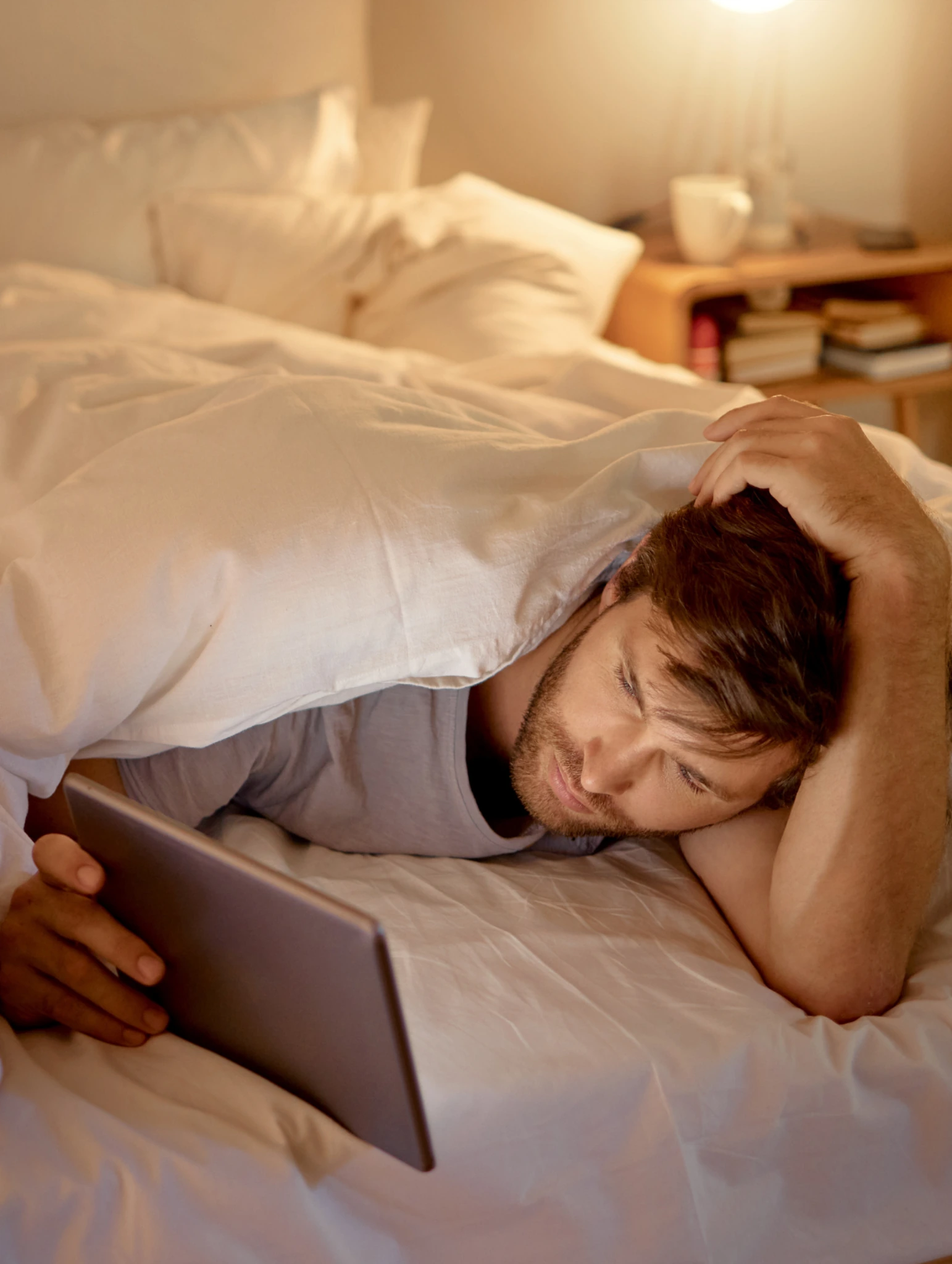 Hombre acostado en la cama mirando una tablet, imagen que representa errores comunes al atravesar las etapas de una relación a distancia y la incertidumbre emocional.