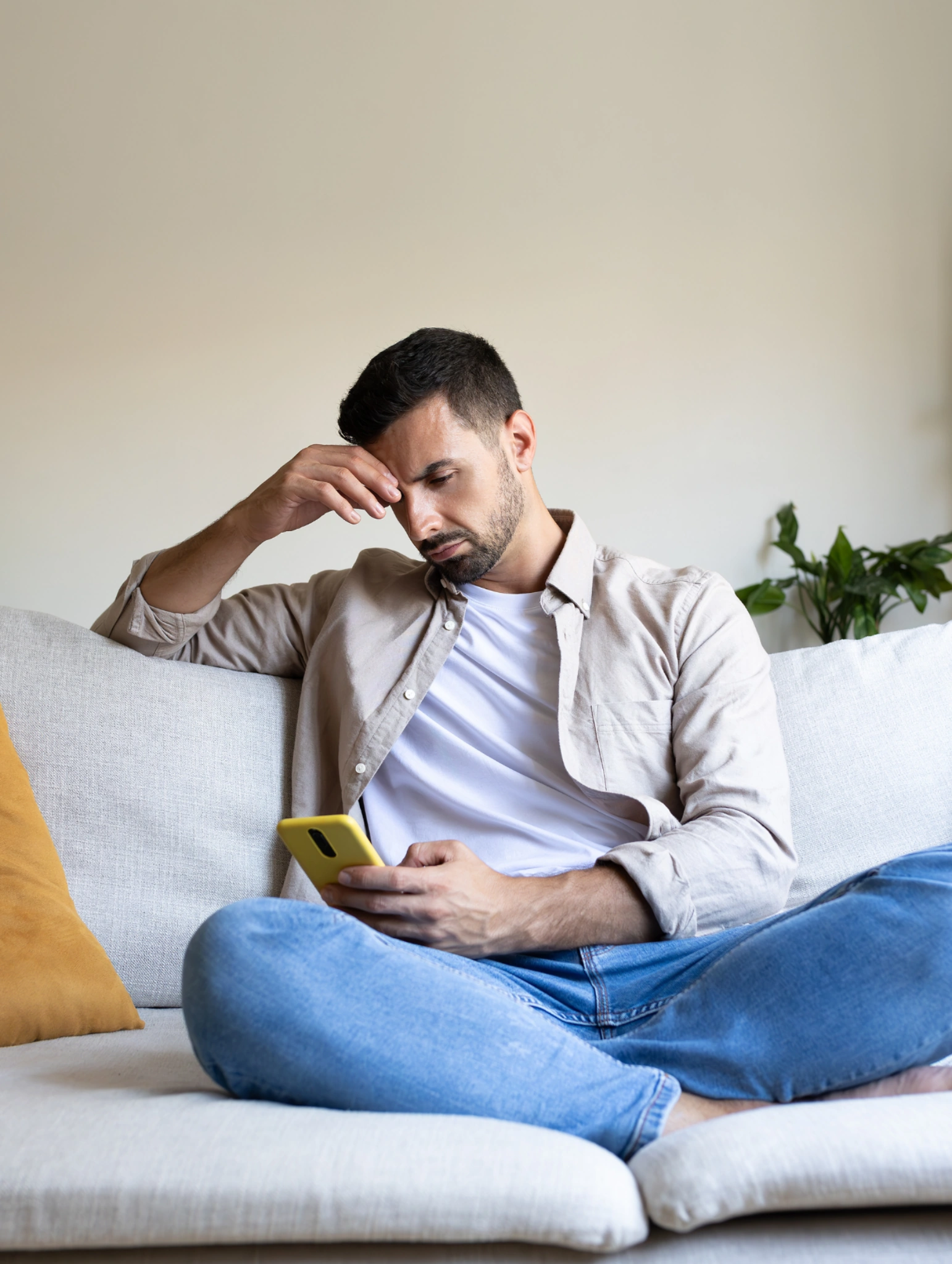 Hombre sentado en un sofá mirando su celular con expresión de preocupación, imagen que representa los 7 indicadores que marcan el final de una relación a distancia.