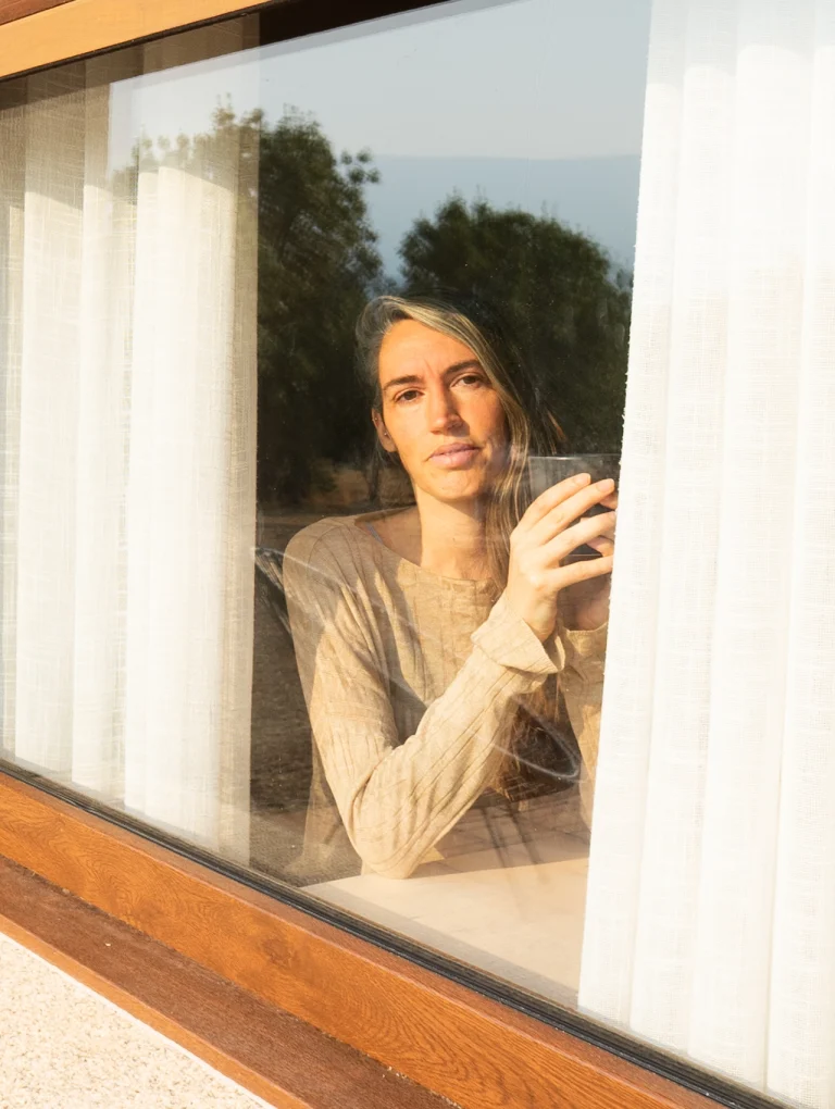 Mujer mirando por la ventana con expresión seria y reflexiva, representando tipos de manipulación emocional en relaciones y estados de introspección emocional.