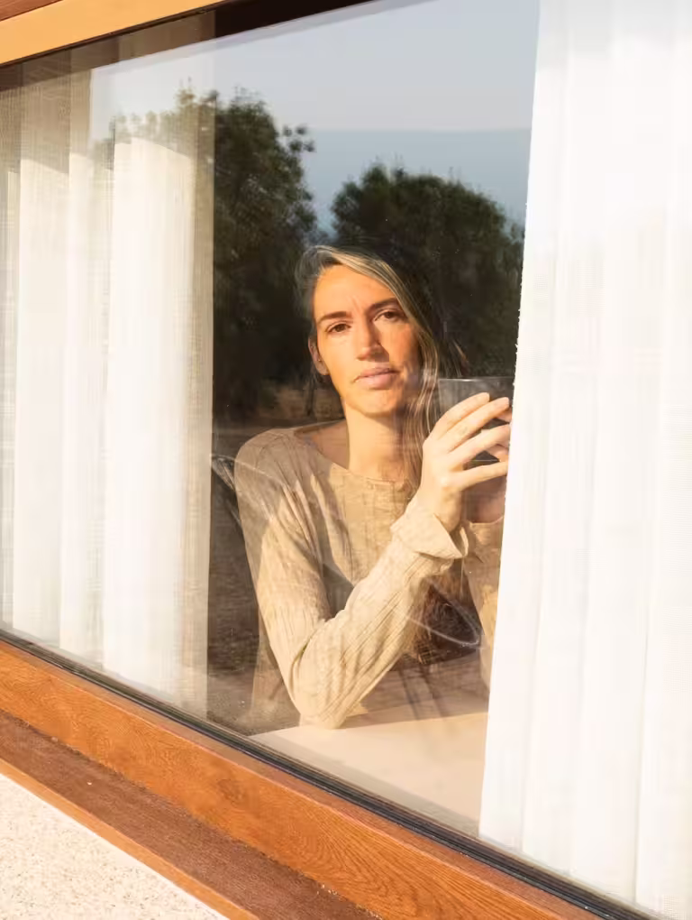 Mujer mirando por la ventana con expresión seria y reflexiva, representando tipos de manipulación emocional en relaciones y estados de introspección emocional.