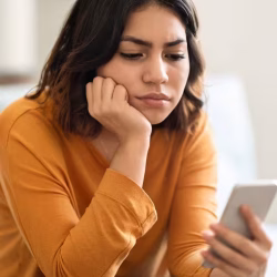 Mujer mirando su celular con expresión triste y pensativa, representando cómo terminar una relación a distancia cuando la conexión emocional comienza a romperse.